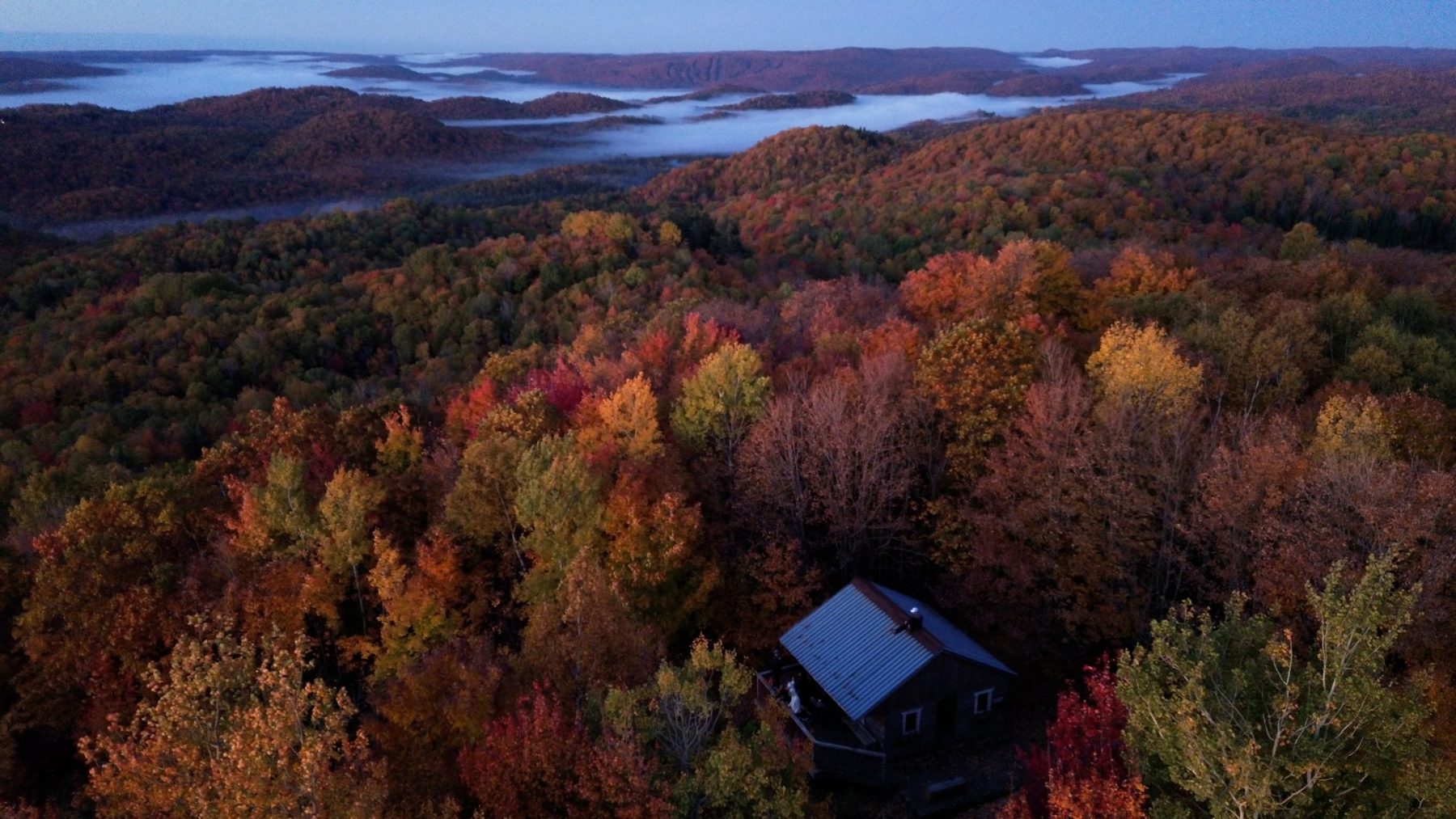 Vue aérienne d'un chalet dans une forêt d'automne, avec de la brume dans les vallées au loin