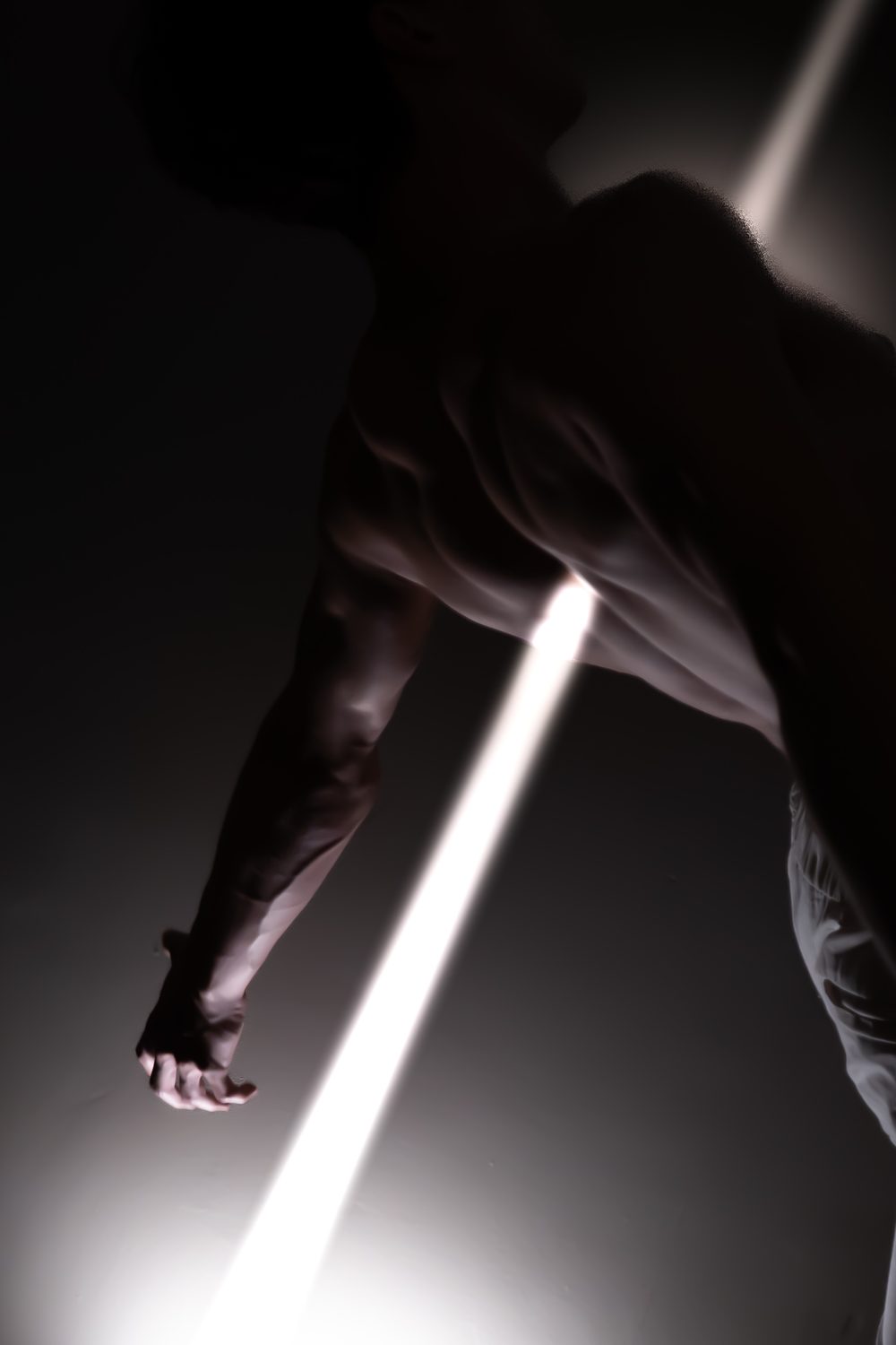 Torse d'un homme dans la pénombre, traversé par un faisceau de lumière blanche